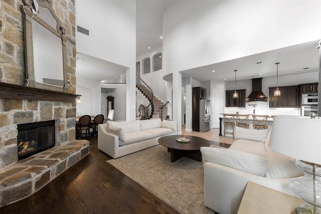 Floor-to-ceiling stone fireplace, dark wood-finish flooring, soaring ceilings, curved staircase with iron railing, and gourmet kitchen with dark cabinetry and breakfast bar