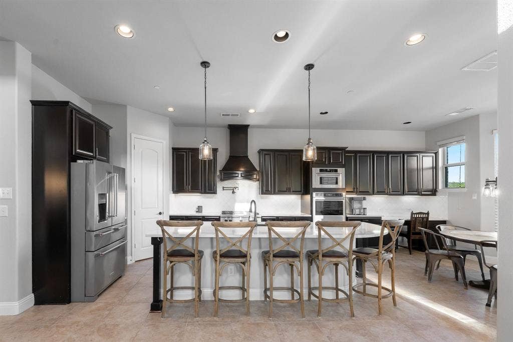 Kitchen featuring dark wood cabinetry, a central stone-topped island with seating, stainless steel appliances, a built-in oven, and recessed lighting