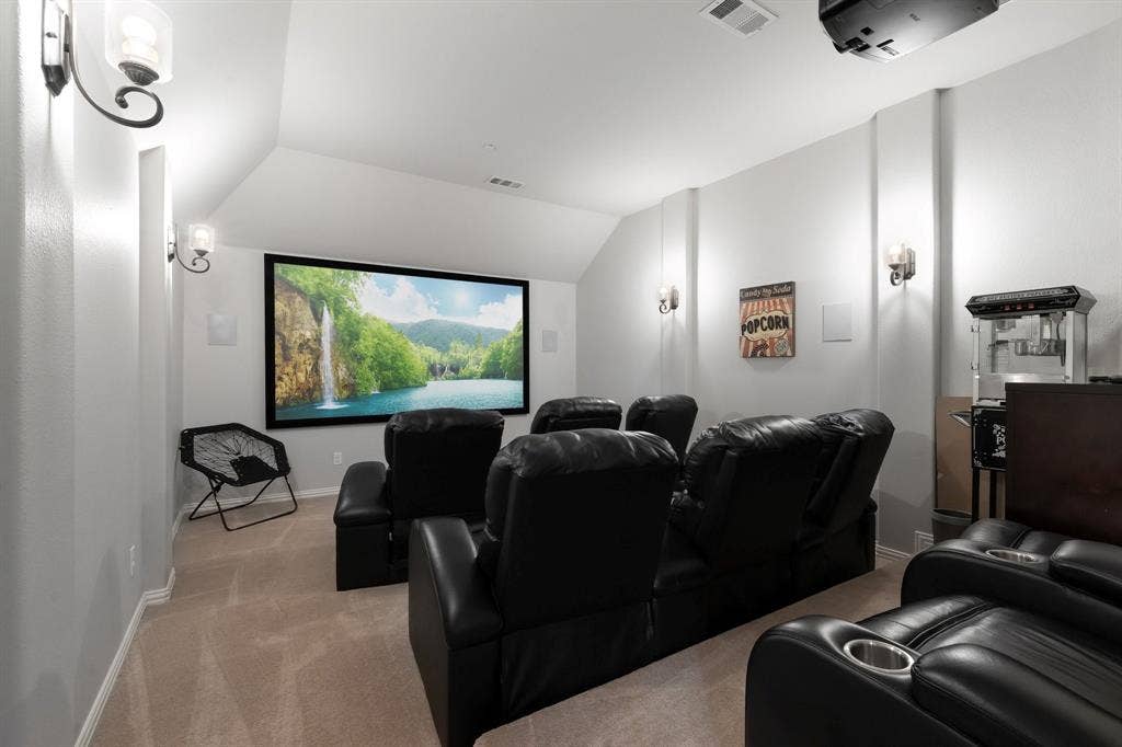 Dedicated room featuring a projector screen, wall-mounted sconce lighting, neutral carpeting, and sloped ceiling architecture