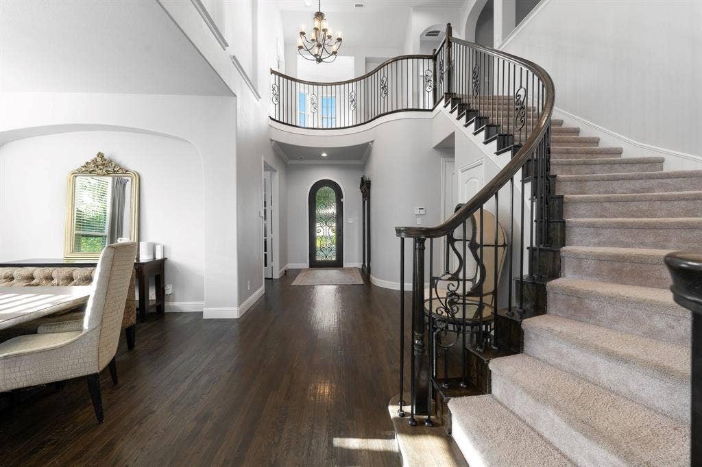Grand foyer featuring a curved staircase with iron balusters, dark wood-finish flooring, an arched entryway with a glass-paneled door, and a multi-tiered chandelier
