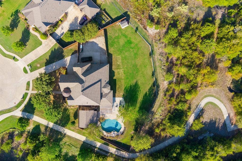 Aerial perspective of a property featuring an in-ground pool, expansive grass lawn, paved driveway, and perimeter wood fencing