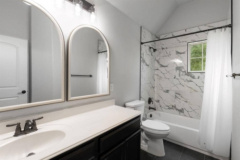 Completely renovated bathroom!  Dark-toned cabinetry with a white countertop, dual arched wall mirrors, and a tub-shower combination featuring large-format stone-patterned tile surrounds