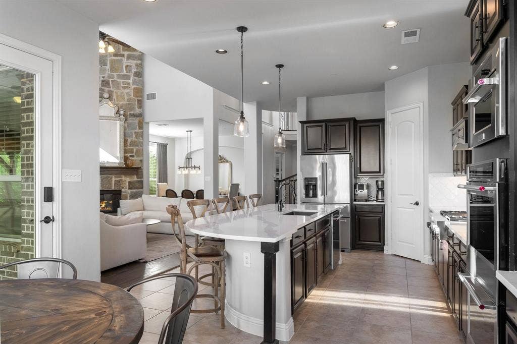 Kitchen featuring a stone-faced fireplace, dark cabinetry, a large island with stone countertop, stainless steel appliances, and recessed lighting