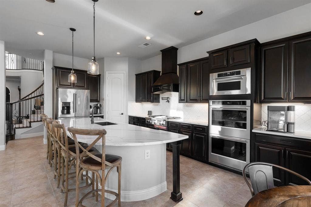 Kitchen featuring dark cabinetry, expansive stone-surface island, stainless steel built-in double wall ovens, recessed lighting, and tile flooring