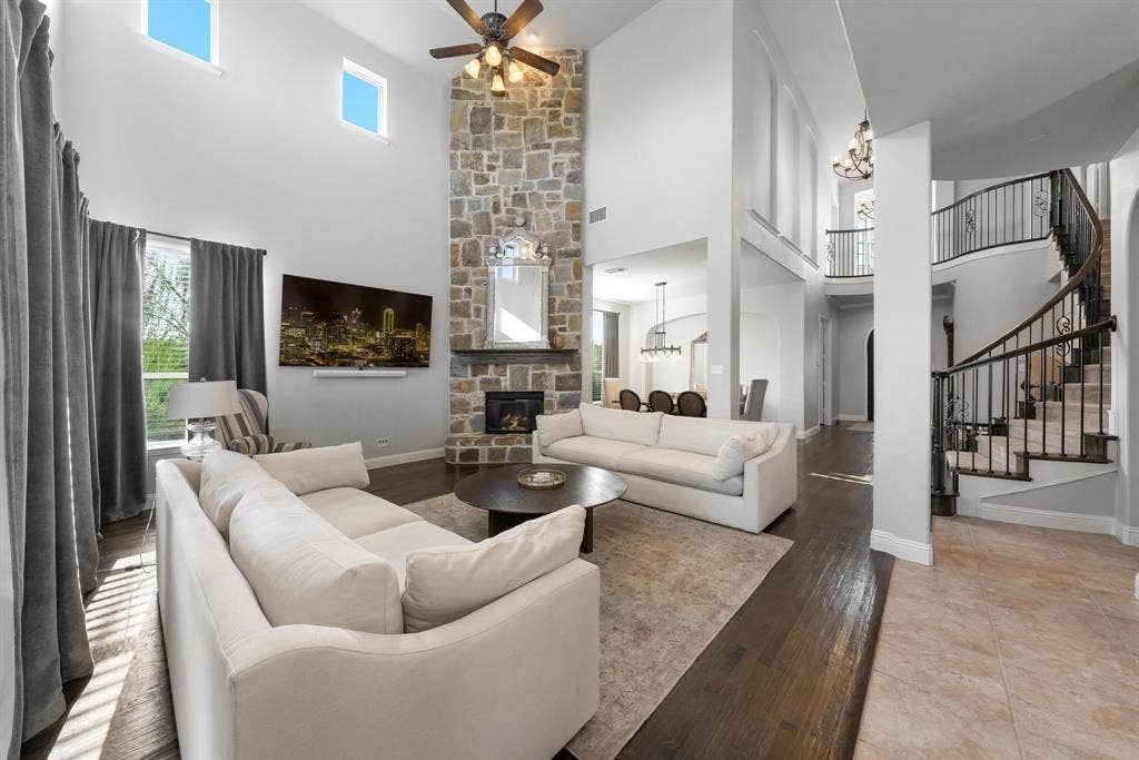 Two-story living area featuring a floor-to-ceiling stone fireplace, wood-finish flooring, double-height ceilings, and a curved staircase with iron balusters