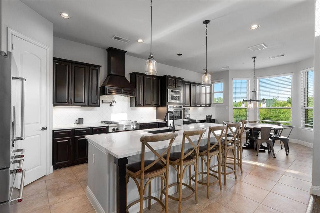 Kitchen featuring dark cabinetry, quartz countertops, a large center island, built-in stainless steel commercial kitchenaid appliances, and tile flooring