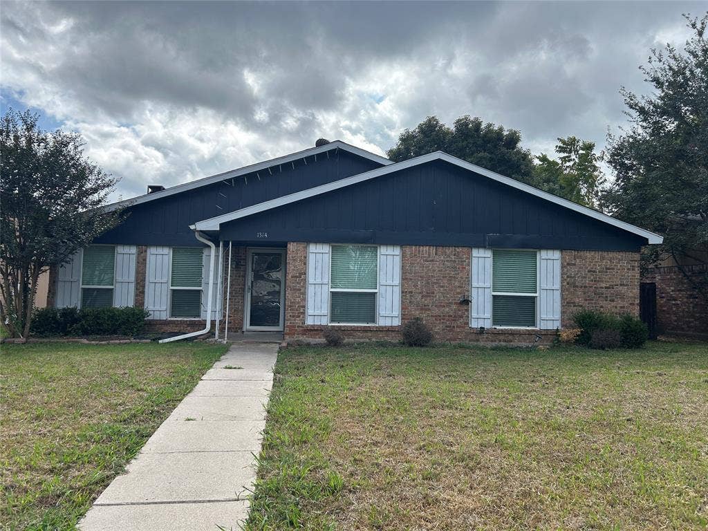 1314 Frio Lane, Garland, TX 75040 Single-story exterior featuring a brick facade, dark-toned horizontal siding, white louvered shutters, and a concrete walkway