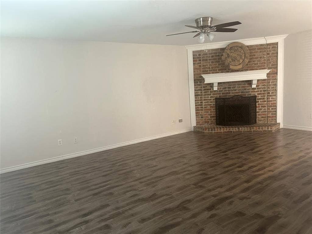 1314 Frio Lane, Garland, TX 75040 Wood-finish flooring, corner brick fireplace with a custom mantle, and a ceiling-mounted light fixture with a fan