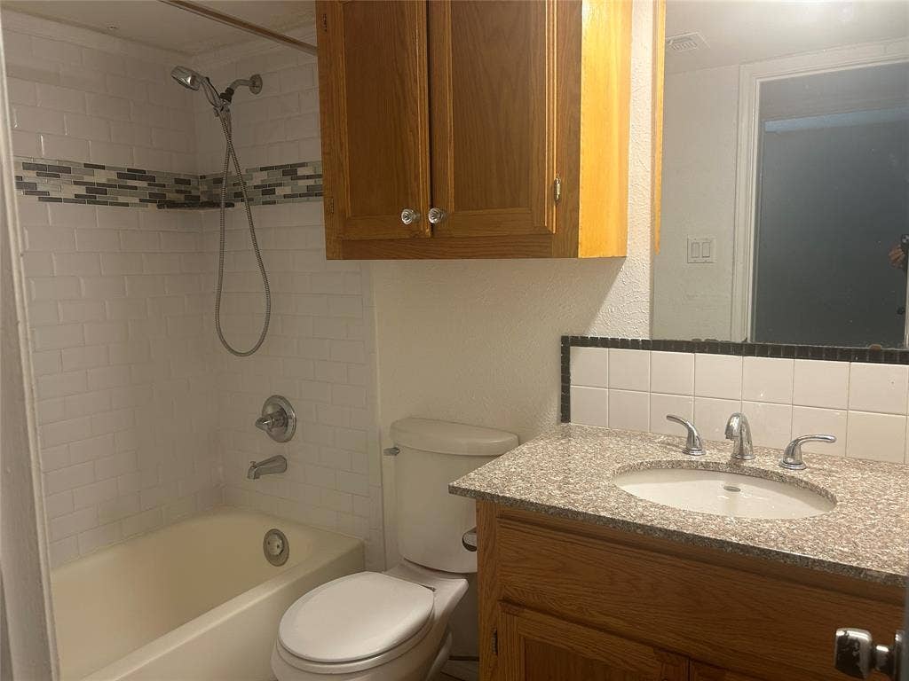 1314 Frio Lane, Garland, TX 75040 Bathroom featuring a wood-finish vanity with a stone-composite countertop, an integrated oval sink, subway tile shower surround with decorative mosaic inlay, and wall-mounted cabinetry