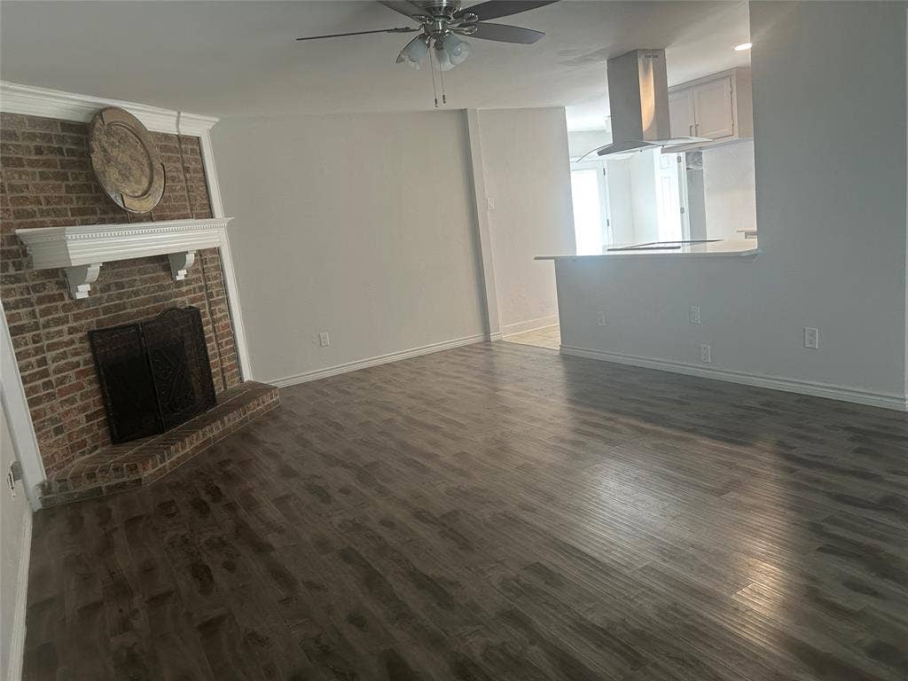 1314 Frio Lane, Garland, TX 75040 Living area featuring wood-finish flooring, a brick fireplace with a decorative mantel, a ceiling fan, and a kitchen breakfast bar with a stainless steel range hood