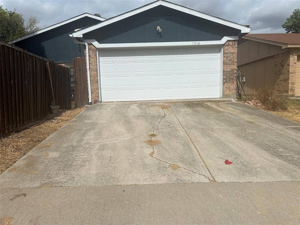 1314 Frio Lane, Garland, TX 75040 Attached two-car garage with white roll-up door, brick masonry siding, and dark-toned exterior cladding