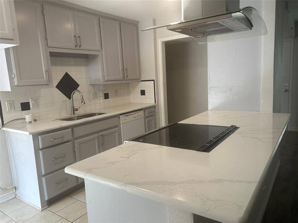 1314 Frio Lane, Garland, TX 75040 Kitchen featuring light-toned cabinetry, solid-surface countertops with veining, an integrated island cooktop, a stainless steel range hood, and a dual-basin undermount sink