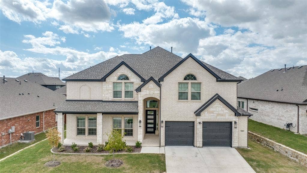 Two-story residence featuring a light-toned brick and stone facade, dual-gabled rooflines, arched window detailing, and an attached two-car garage