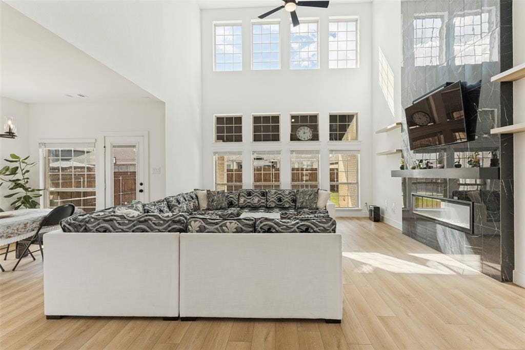 Double-height ceilings, floor-to-ceiling stone-finish fireplace, built-in horizontal shelving, wood-finish flooring, and expansive grid windows