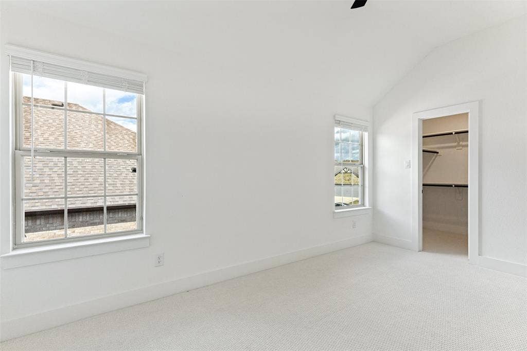 Vaulted ceiling, wall-to-wall carpeting, dual windows with grid detailing, and a walk-in closet with built-in shelving