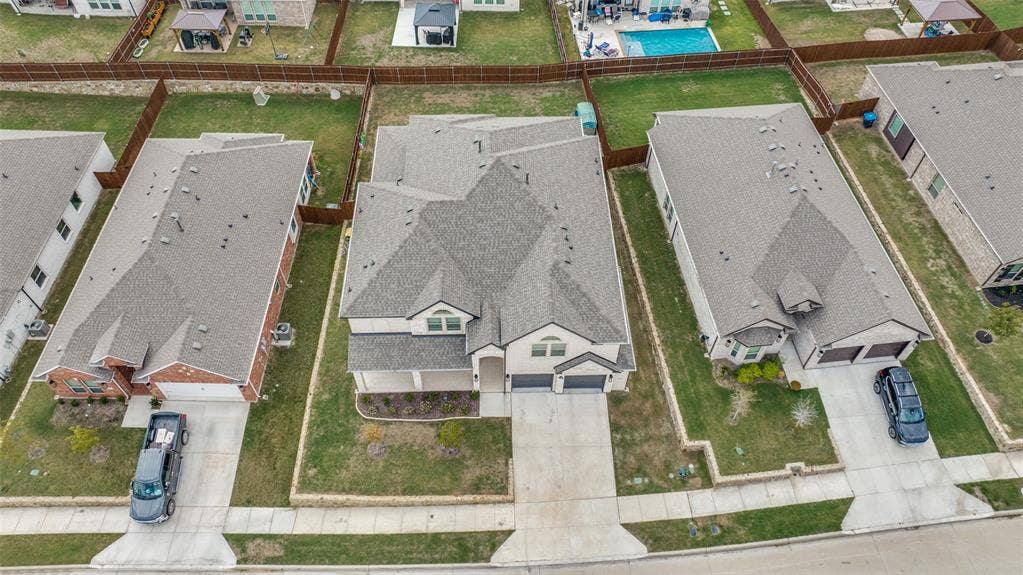 Aerial perspective of a multi-gabled residence featuring a multi-car garage, concrete driveway, and a fenced rear lawn