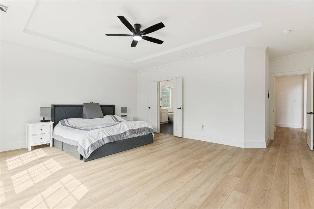 Tray ceiling with a central matte black ceiling fan, wood-finish flooring, and double-door entry