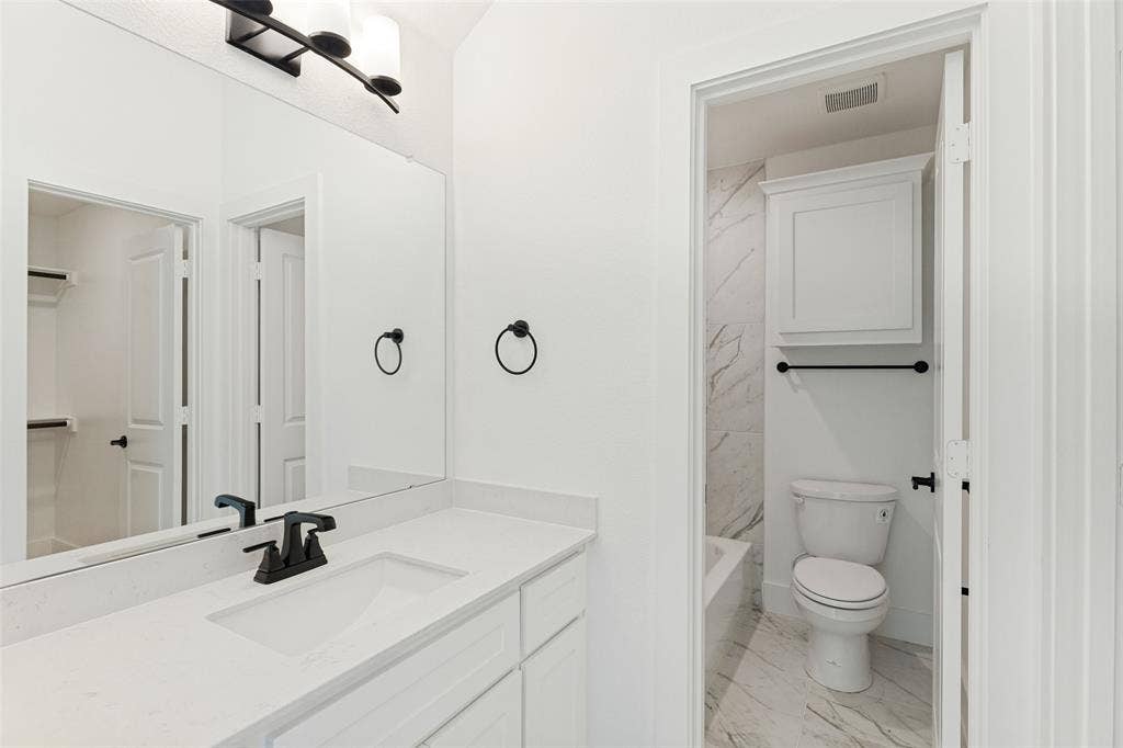 Bathroom featuring a vanity with a stone countertop, an integrated rectangular sink, matte black plumbing fixtures, an expansive wall-to-wall mirror, and overhead lighting