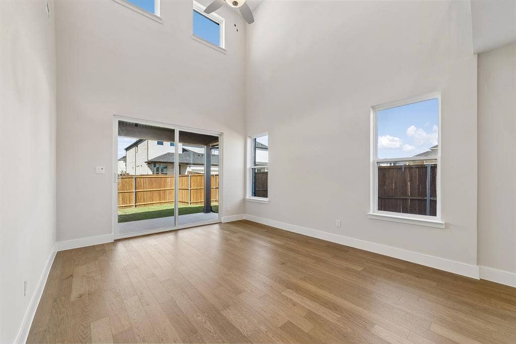 Volume ceiling with multi-level windows, wood-finish flooring, sliding glass door, and ceiling fan