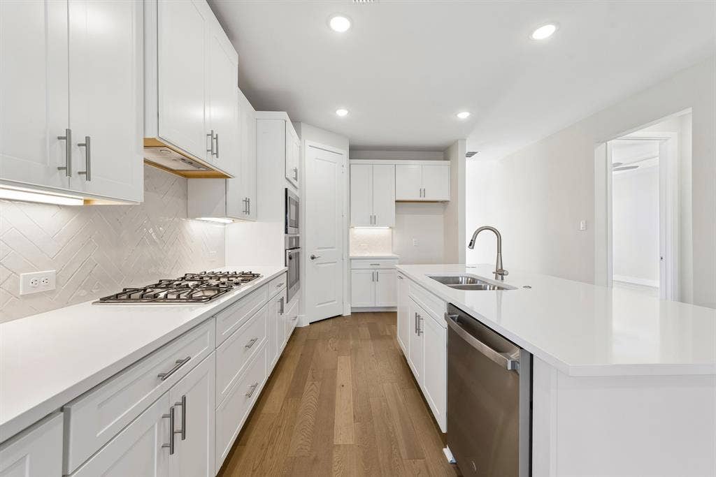 Kitchen featuring white shaker-style cabinetry, solid-surface countertops, a herringbone-patterned tile backsplash, stainless steel appliances, and wood-finish flooring