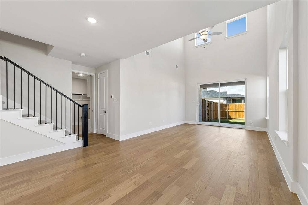 High-ceiling interior featuring wood-finish flooring, metal staircase railing, ceiling fan, and sliding glass door