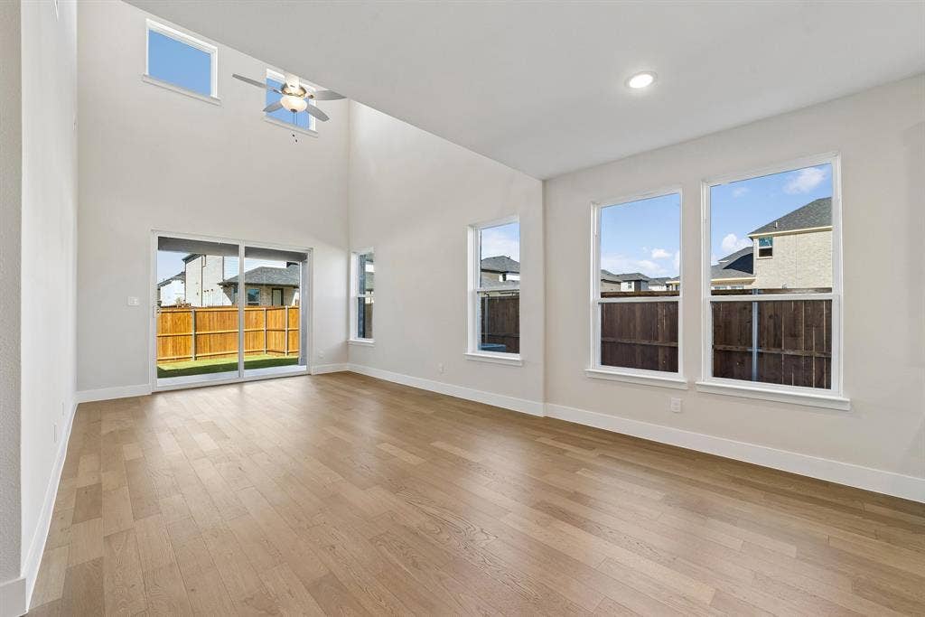 High-ceiling interior featuring wood-finish flooring, recessed lighting, a ceiling fan, and large windows with sliding glass door access to the exterior