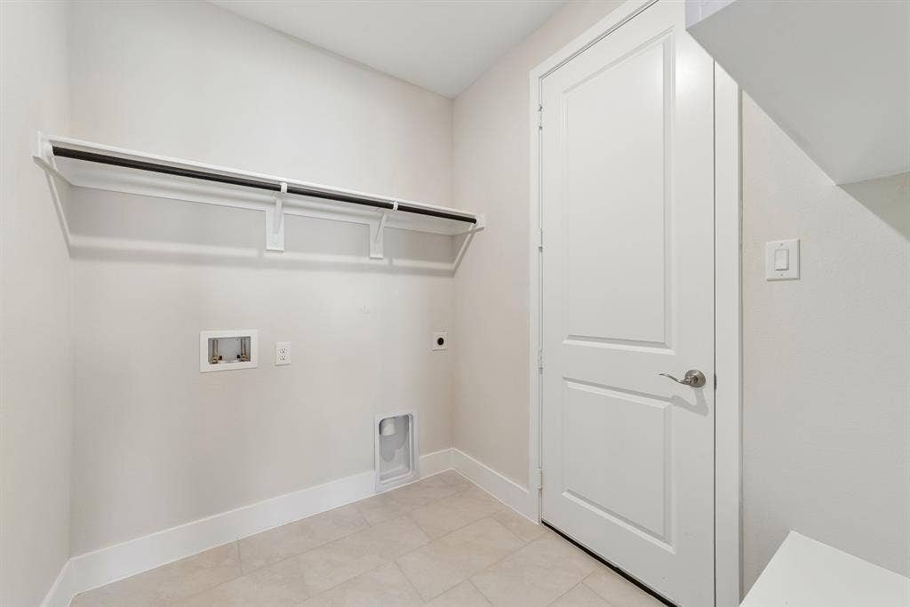 Utility area featuring neutral tile flooring, built-in wall shelving, a solid-core interior door with satin nickel hardware, and dedicated hookups for laundry appliances