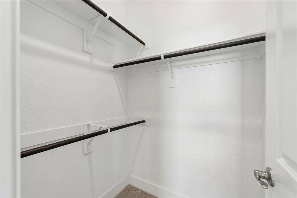 Storage area featuring tiered white shelving and dark-finish clothing rods