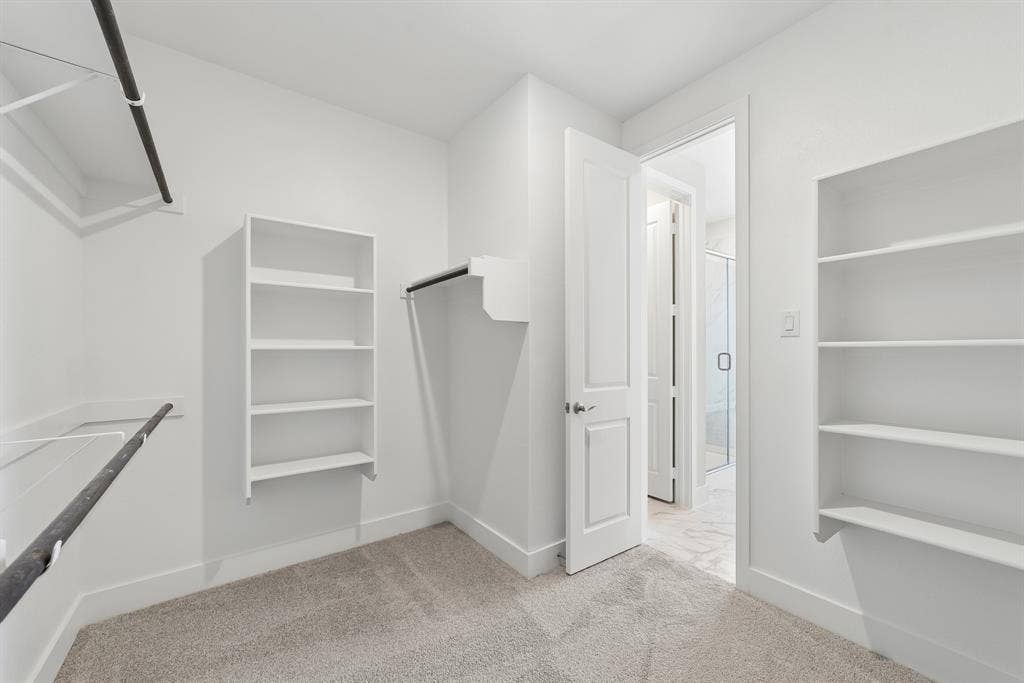 Walk-in closet featuring wall-to-wall carpeting, white shelving units, and dual hanging rods