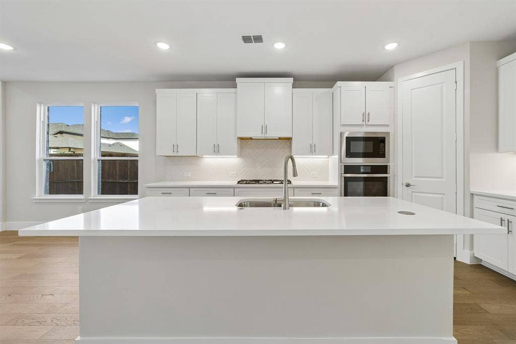 Kitchen featuring white cabinetry, quartz countertops, a central island with an undermount sink, built-in double wall ovens, and wood-finish flooring