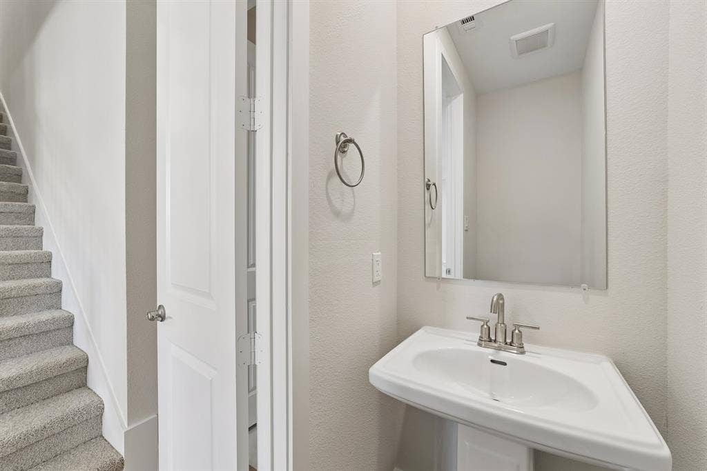 Wall-mounted vanity featuring a pedestal basin, dual-handle metal faucet, rectangular mirror, and circular towel ring