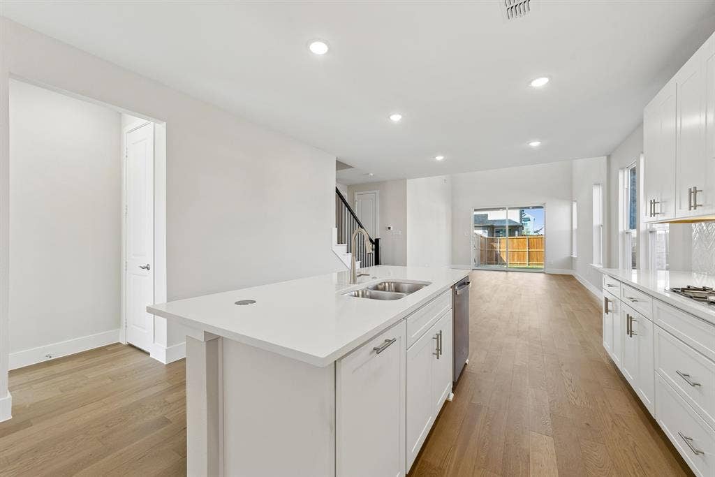 Kitchen featuring white cabinetry, solid surface countertops, a central island with an integrated stainless steel dual-basin sink, recessed lighting, and wood-finish flooring