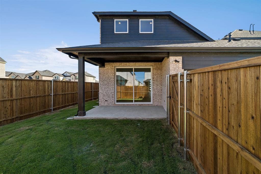 Exterior backyard featuring a covered concrete patio, vertical siding, brick veneer, and a full-perimeter wood fence