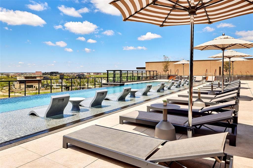 Rooftop infinity-edge pool featuring a Baja shelf, tiled deck surfacing, and metal perimeter railing