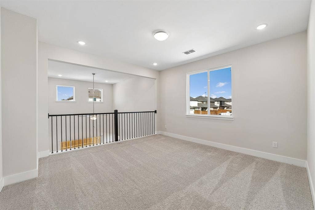 Neutral-toned wall paint, neutral carpeting, recessed ceiling lighting, and black metal spindle railing