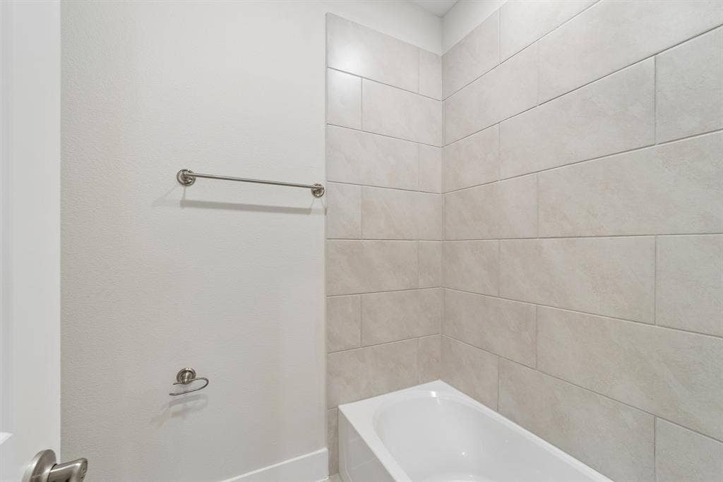 Bathtub featuring full-height neutral-toned rectangular tile surround, matte finish metal towel bar, and coordinated metal toilet paper holder