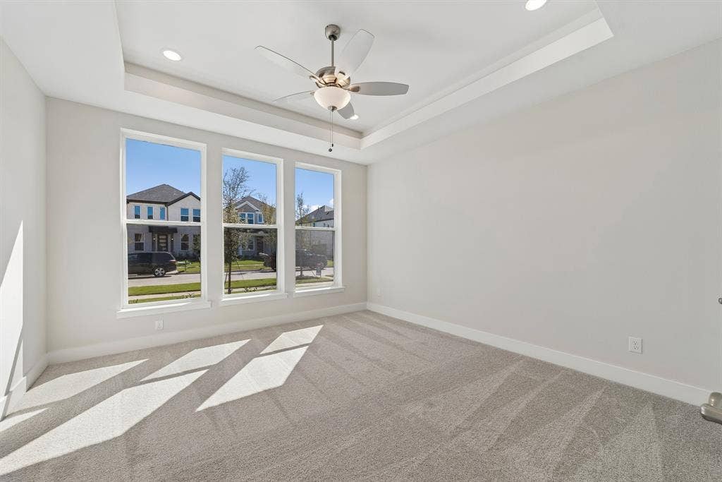 Tray ceiling featuring a central brushed-nickel ceiling fan with integrated lighting, triple window configuration, neutral carpeting, and recessed ceiling lighting