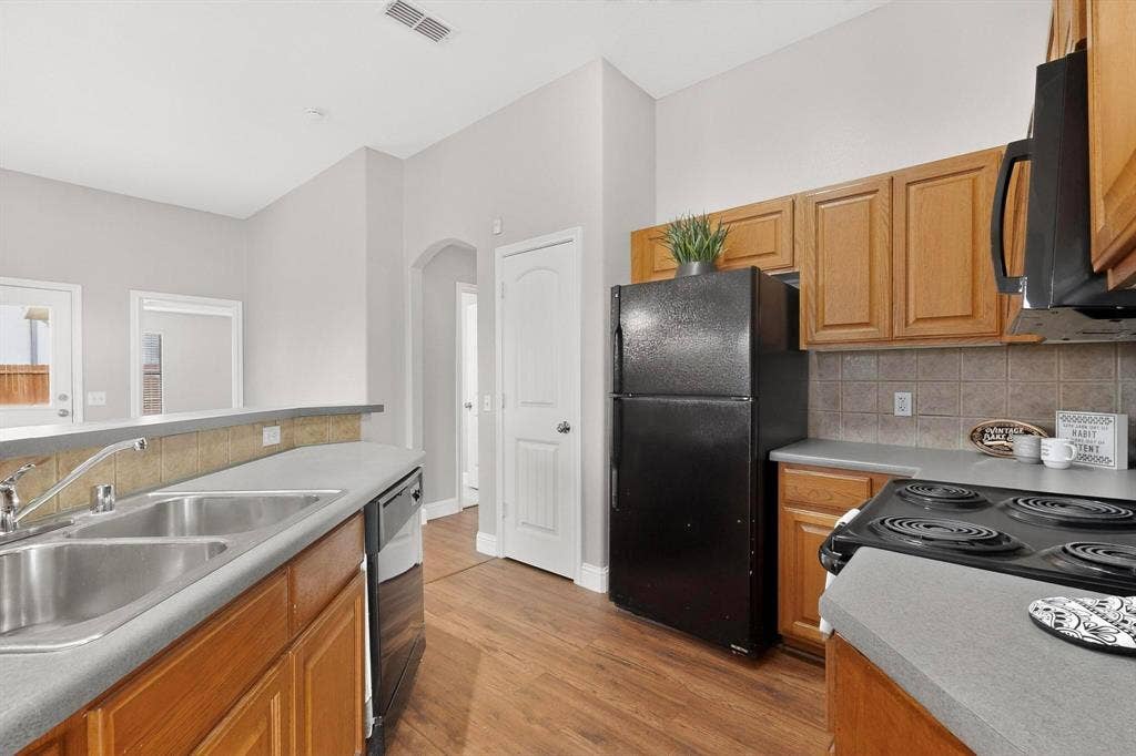 4803 Silver Avenue, Dallas, TX 75223 Kitchen featuring wood cabinetry, solid surface countertops, dual-basin stainless steel sink, black appliances, and wood-finish flooring