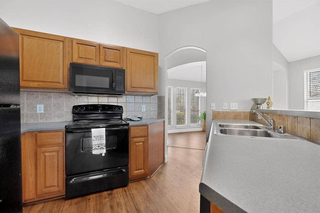 4803 Silver Avenue, Dallas, TX 75223 Kitchen featuring wood cabinetry, solid surface countertops, a tiled backsplash, a double-basin stainless steel sink, and a black appliance package