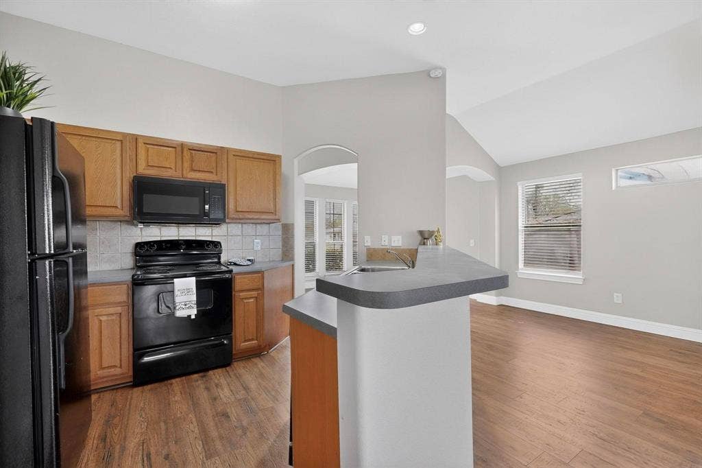 4803 Silver Avenue, Dallas, TX 75223 Kitchen featuring wood cabinetry, solid surface countertops, wood-finish flooring, vaulted ceilings, and an arched entryway