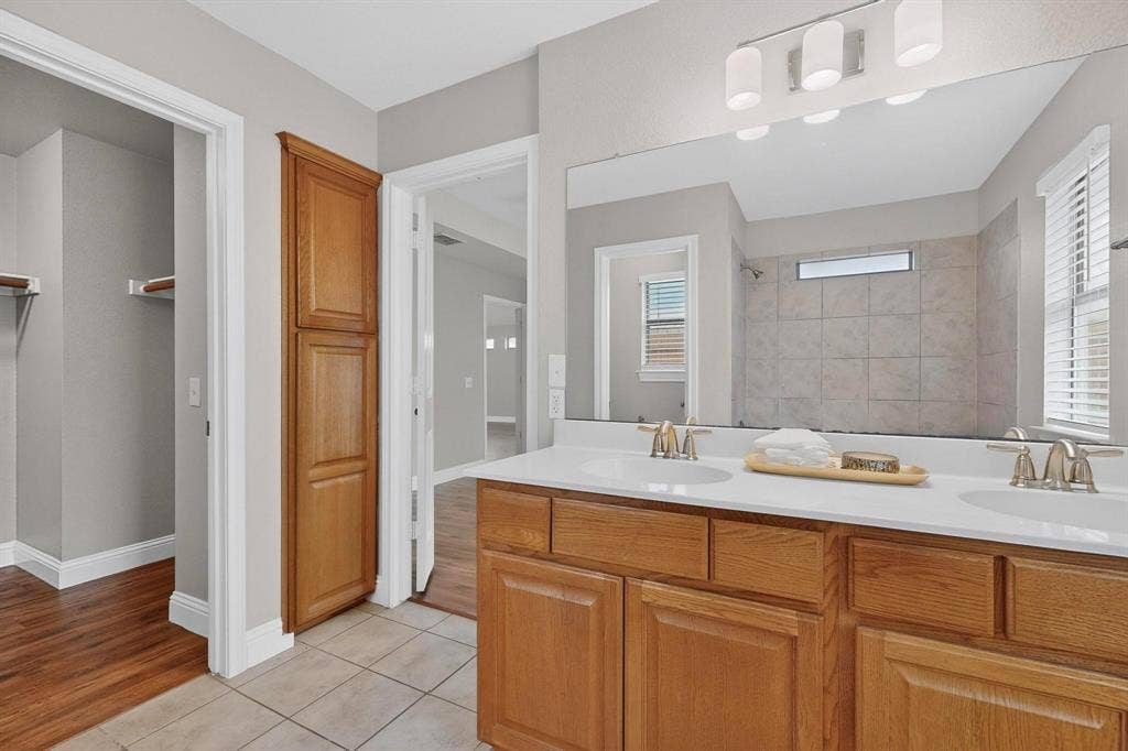 4803 Silver Avenue, Dallas, TX 75223 Dual vanity with solid surface countertop, wood cabinetry, built-in floor-to-ceiling storage, large wall-mounted mirror, and multi-bulb vanity light fixture