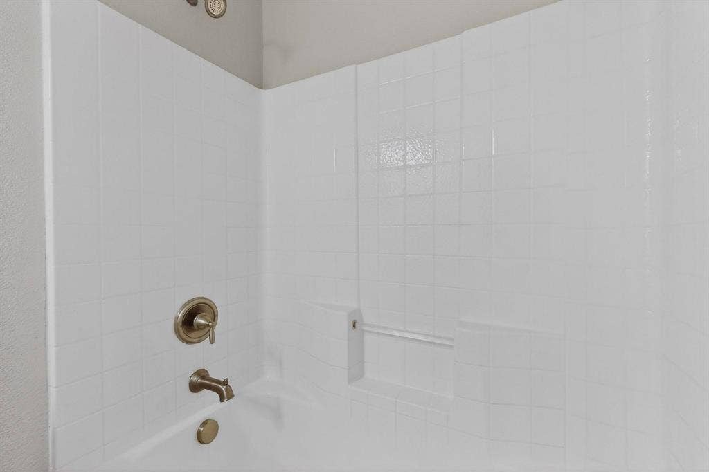 4803 Silver Avenue, Dallas, TX 75223 Bathtub surround featuring white square tiling, integrated shelving, and a bronze-tone plumbing fixture set including a shower head, faucet, and drain control