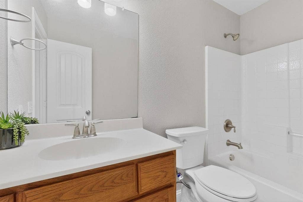 4803 Silver Avenue, Dallas, TX 75223 Bathroom featuring a wood-finish vanity with a solid-surface countertop, a large wall-mounted mirror, and a shower-tub combination with a tiled surround