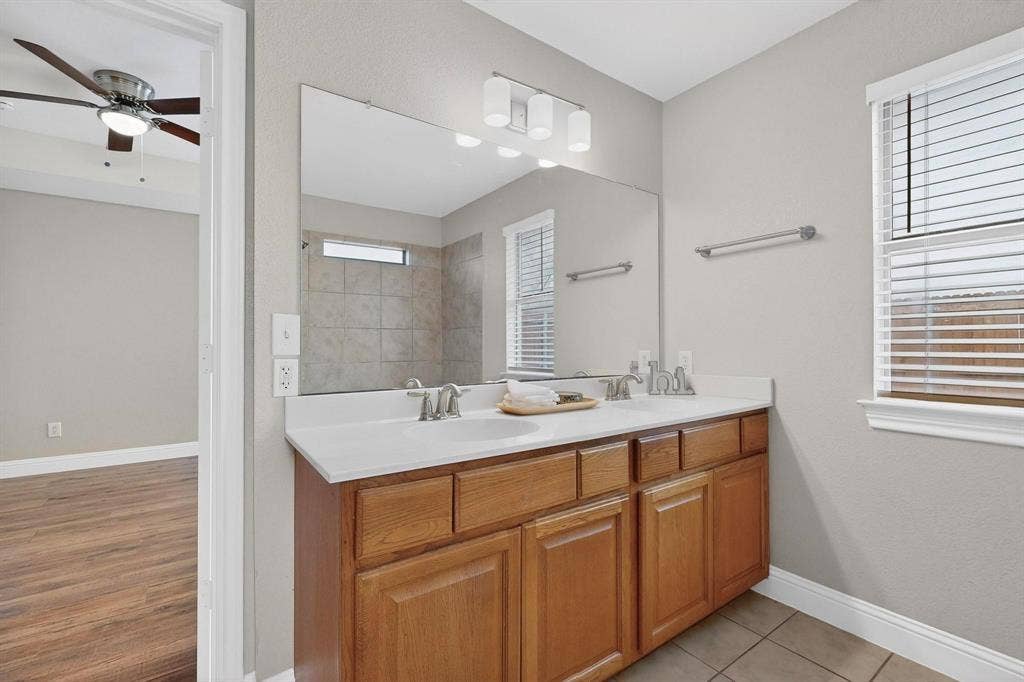 4803 Silver Avenue, Dallas, TX 75223 Dual-sink vanity with light-tone solid surface countertop, wood cabinetry, large vanity mirror, three-light fixture, and tiled flooring