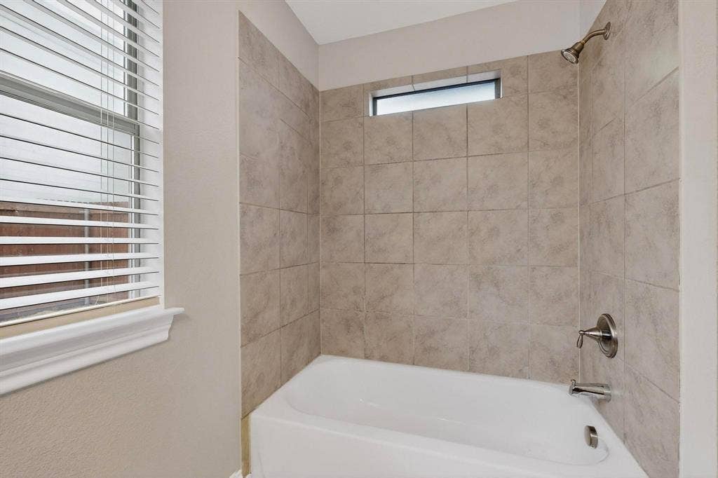 4803 Silver Avenue, Dallas, TX 75223 Bathtub featuring ceramic tile surround, metallic plumbing fixtures, horizontal clerestory window, and operable window with blinds