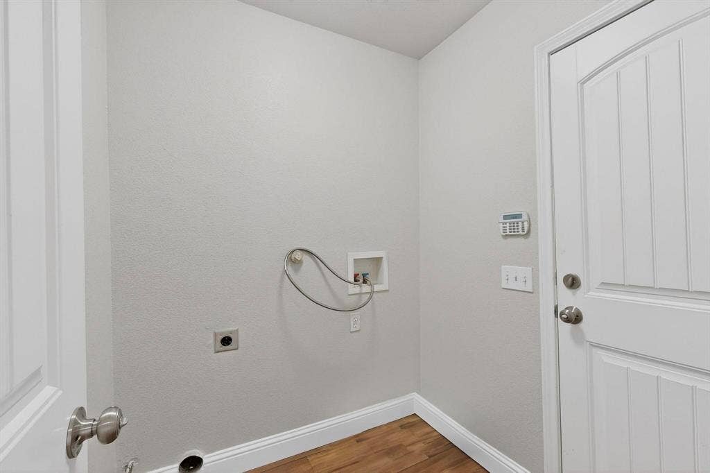 4803 Silver Avenue, Dallas, TX 75223 Utility area featuring wood-finish flooring, recessed water supply box, integrated wall-mounted security keypad, and a six-panel door with brushed nickel hardware