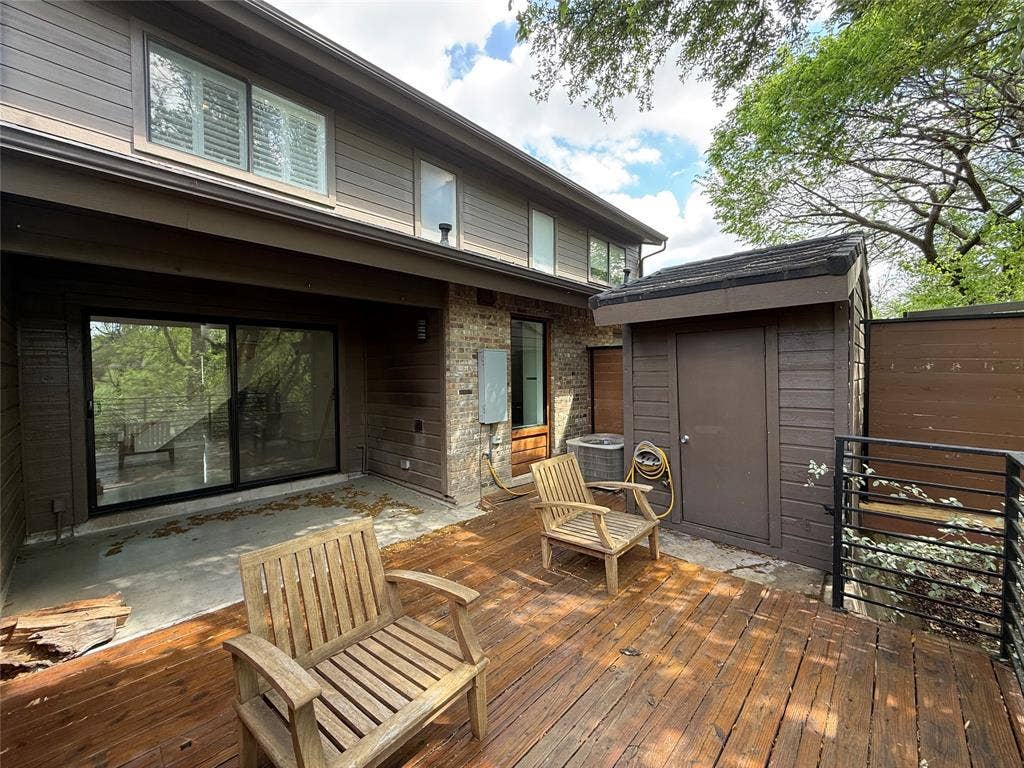 Multi-level wood deck with horizontal railing, brick exterior cladding, sliding glass doors, and attached exterior storage structure