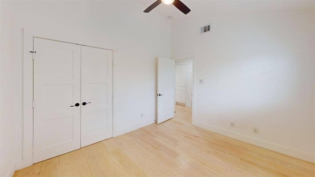 Interior space featuring wood-finish flooring, vaulted ceilings, double-panel closet doors with matte black hardware, and an integrated ceiling fan