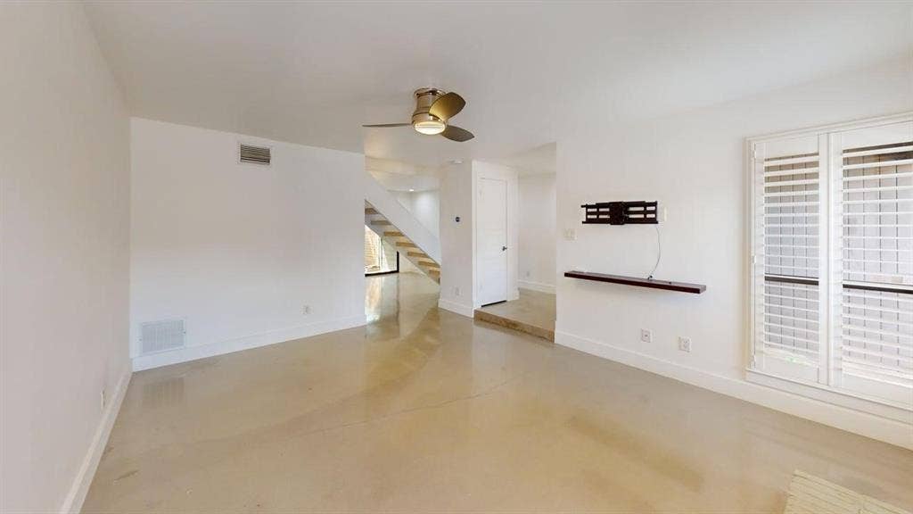 Polished concrete flooring, ceiling fan with integrated lighting, wall-mounted floating shelf, and plantation shutters