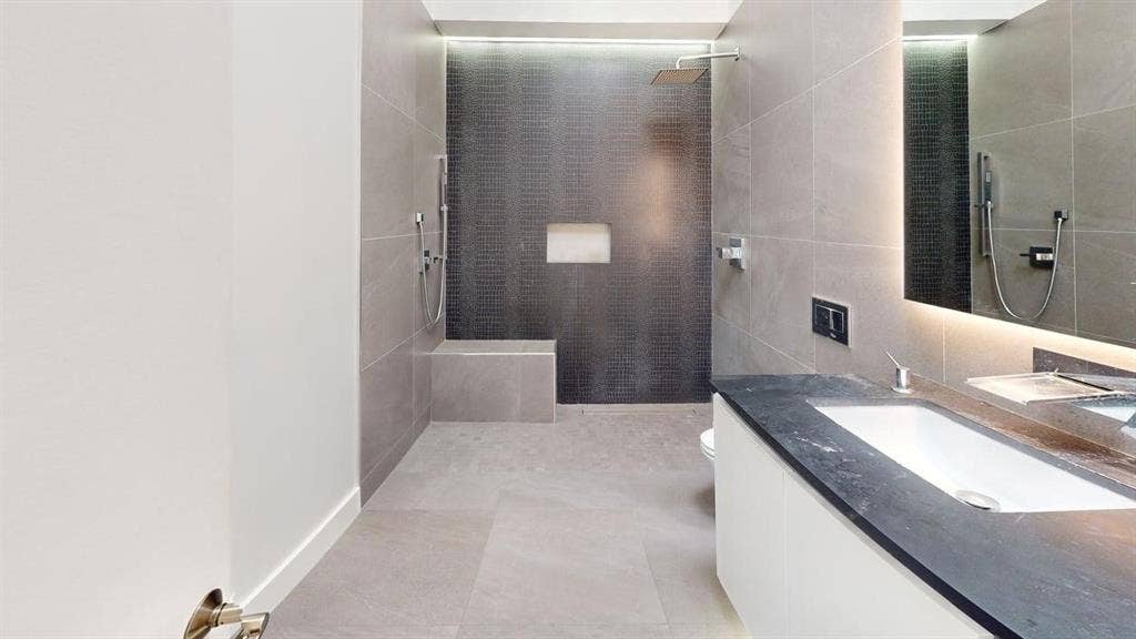 Bathroom featuring a walk-in shower with large-format tile surround, integrated shower bench, and a modern floating vanity with a dark countertop and undermount sink